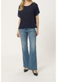 Haut ample bleu marine à manches courtes, associé à un jean évasé délavé et des chaussures noires à talons. Tissu doux et design décontracté.