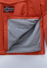 Orange jakke med en struktureret grå foring, synlig gennem en åben lomme, prydet med et rektangulært mærke, der viser det islandske flag.