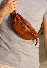 Brown leather fanny pack with multiple zippered pockets, showing a smooth texture and a slightly rounded shape, worn across the torso.