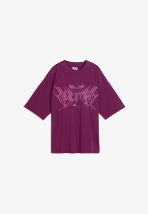 T-shirt oversize violet avec un motif rose style tribal et un logo Puma blanc centré sur la poitrine, manches courtes et col rond.