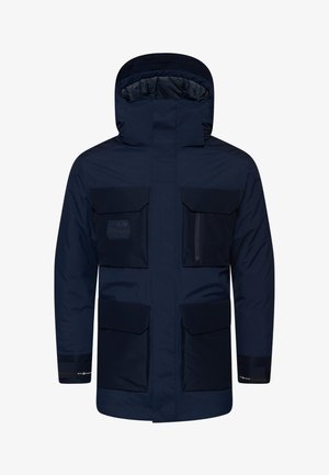Námořnická modrá nepromokavá parka s kapucí, vybavená čtyřmi velkými předními kapsami a zipovou kapsou na hrudi. Zpevněné manžety a brandingový detail.