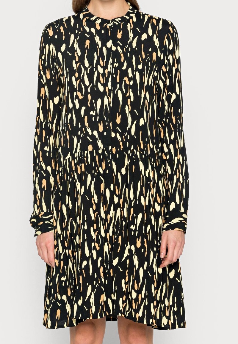 Robe noire à manches longues avec des taches abstraites jaunes et marron clair, boutonnée sur le devant et taille froncée.