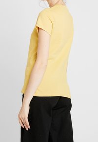 Żółta bawełniana koszulka z krótkim rękawem, okrągłym dekoltem i dopasowanym krojem. Połączona z czarnymi spodniami o wysokim stanie, o gładkiej fakturze.