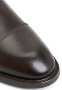Scarpa in pelle marrone con punta arrotondata, dettagli cuciti nella parte anteriore e una finitura liscia. Presenta una suola resistente con un leggero lucido.
