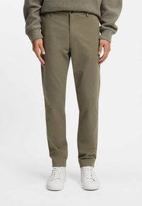 Olivengrønne skræddersyede bukser med lige pasform og subtil tekstur; har knaplukning og frontlommer, parret med hvide sneakers.
