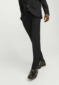 Czarne dopasowane spodnie o gładkiej fakturze, zestawione z wypolerowanymi czarnymi eleganckimi butami z wzorem brogue.