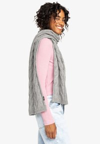 Écharpe en tricot gris, avec une texture douce, un look superposé et des détails cousus, portée par-dessus un haut côtelé rose clair.