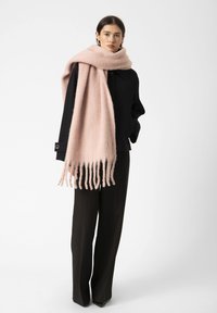 Bufanda de lana rosa con bordes deshilachados, combinada con un abrigo negro y pantalones negros. La tela parece suave y texturizada.