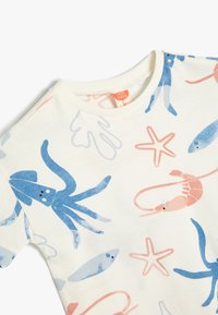 Kortærmet børnet-shirt i blød, cremefarvet bomuld med mønstre af blå blæksprutter, pink rejer og fisk. Rund halsdesign.
