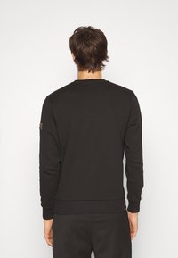 Felpa nera a girocollo realizzata in materiale misto cotone. Presenta maniche lunghe, polsini a coste e un patch con logo sulla spalla sinistra.