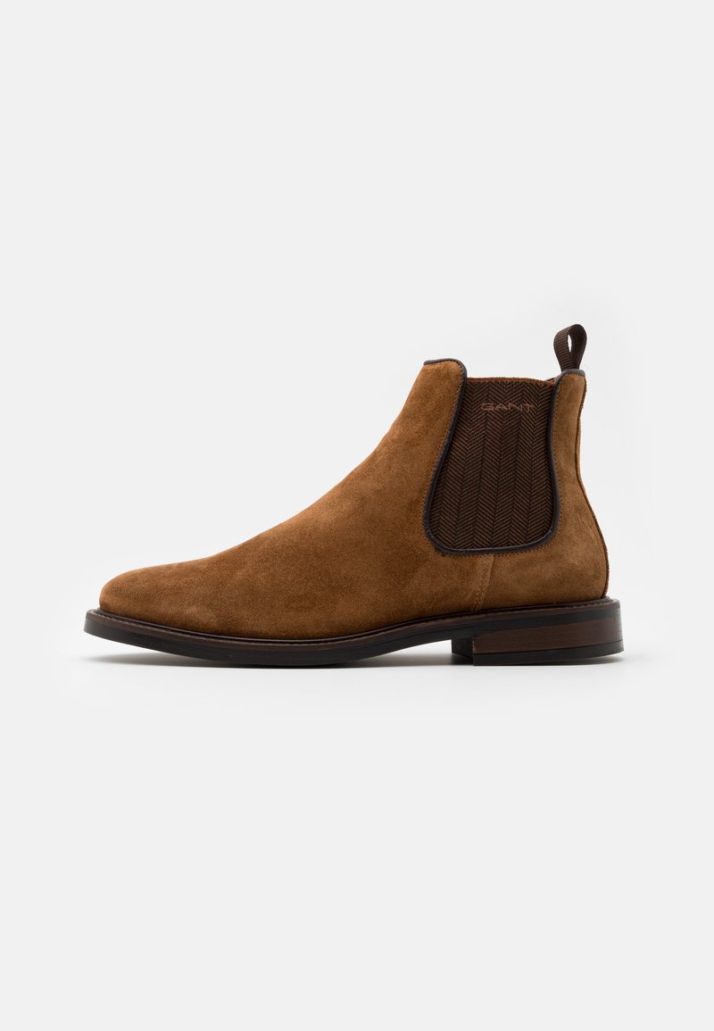 Botte Chelsea en daim marron avec panneau latéral élastique foncé, languette au talon, et semelle en bois empilée basse.
