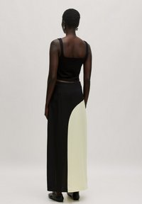 Zwarte geribbelde cropped top gecombineerd met een lange rok met aan één kant een crèmekleurig gedeelte, gemaakt van een zachte stof en met een relaxte pasvorm.