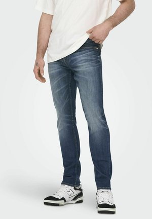 Temno modre jeans hlače ravnega kroja, z lahkim efektom zbledelosti, petimi žepi in kontrastnim šivanjem. Nosi se z belo majico in športnimi copati.