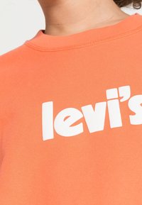 Sudadera de algodón naranja con textura acanalada, con un logotipo "levi's" impreso en blanco en el pecho. Cuello alto, ajuste informal.