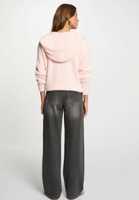 Felpa con cappuccio rosa e soffice, con dettagli a trecce sulle maniche, abbinata a jeans a gamba larga in denim grigio scuro.