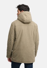 Kaki kordfløyeljakke med stor hette, med vertikal ribbet tekstur og rett snitt, sett fra baksiden.