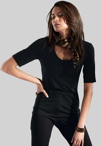 Schwarzes kurzärmliges Oberteil mit Rundhalsausschnitt, kombiniert mit schwarzen Hosen. Ein Leoprint-Schal verleiht dem Outfit Detail um den Hals. Glatte Textur.