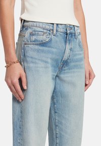 Jeans de mezclilla azul claro con un corte relajado, cintura alta y costuras visibles. Presenta bolsillos frontales y un ligero desgaste en la tela.