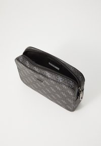 Bolso negro texturizado con patrón de logotipos metálicos, cierre de cremallera, forma rectangular y un pequeño acento plateado en la cremallera.