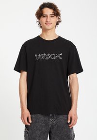 Black cotton t-shirt with a crew neckline, featuring a white graphic logo "VOLCOM" in a stylized font across the chest and short sleeves.
