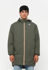 Parka vert olive avec capuche, dotée d'une fermeture éclair avec une rayure multicolore et d'un logo sur la poitrine. Doublure douce visible au niveau du col.