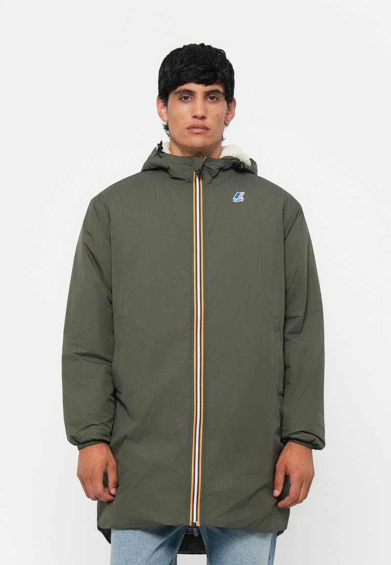 Parka vert olive avec capuche, dotée d'une fermeture éclair avec une rayure multicolore et d'un logo sur la poitrine. Doublure douce visible au niveau du col.