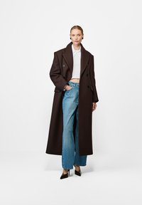 Brązowy płaszcz podwójnie zapinany z dużymi klapami, noszony na białej, krótkiej bluzce. W połączeniu z jasnoniebieskimi spodniami o szerokich nogawkach i czarnymi, spiczastymi szpilkami.