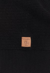 Beanie nera in maglia con tessuto testurizzato, con bordo inferiore a costine e un'etichetta in pelle marrone che riporta "KEY LARGO" e il logo.