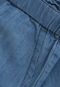 Niebieska tkanina dżinsowa o teksturowanej powierzchni, z marszczonym elastycznym paskiem w talii i widocznymi detalami szwów.