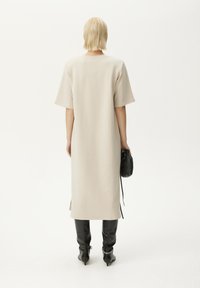 Beige mekko polven pituudelta, jossa on lyhyet hihat, sileä rakenne, sivuaukot ja rento istuvuus. Yhdistetty mustiin polvisukkiin ja pieneen mustaan laukkuun.