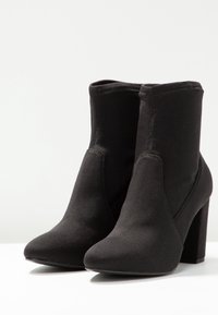 Botines negros de tobillo hechos de un tejido suave, con punta afilada y tacón cuadrado, que presentan una textura lisa y mínimos detalles de costura.