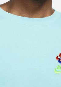 T-shirt in cotone azzurro chiaro con scollo rotondo, caratterizzata da un logo ricamato multicolore sul petto nei colori rosso, blu e verde.