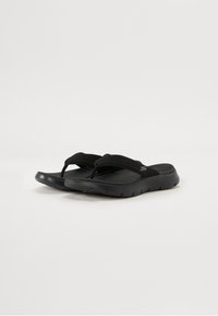 Black flip-flops featuring a textured fabric strap, contoured sole, and flexible rubber outsole for comfort. Simple and minimalistic design.