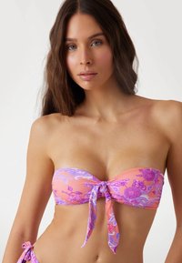 Strapless bikini top in pink fabric with purple floral patterns; features a center tie and smooth texture.