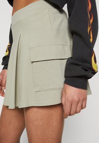 Světle zelený šortkový sukňový kousek vyrobený z měkké tkaniny s sklady, disponující boční kapsou a hladkou texturou.