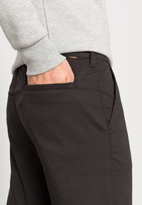 Black trousers with a smooth texture, featuring a side pocket and subtle stitching details. Paired with a light gray, ribbed sweatshirt.