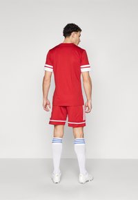 Rode sporttrui met witte strepen, bijpassende rode shorts en witte sokken met blauwe strepen, allemaal vervaardigd uit lichtgewicht stof.