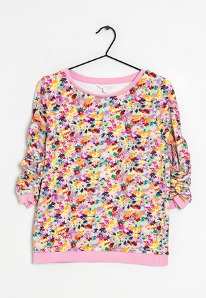 Langärmliges Oberteil mit gerafften Ärmeln, das ein buntes Blumenmuster und rosa Besatz am Ausschnitt, an den Bündchen und am Saum zeigt, aufgehängt an einem schwarzen Kleiderbügel.