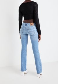 Blå denimjeans med lätt utsvängning, med en varumärkeslapp vid midjan och synliga söm detaljer. Kombinerat med en svart spets topp med långa ärmar.