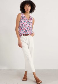 Top senza maniche floreale con scollo a V nei colori rosa, blu e bianco, abbinato a pantaloni bianchi a gamba larga e sandali marroni con cinturini.