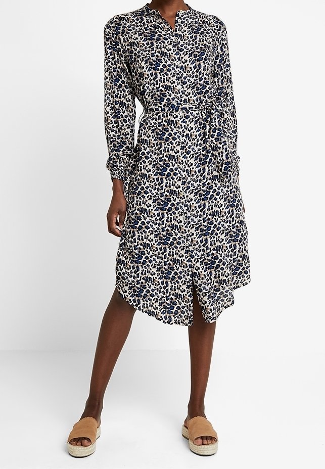 Klänning med leopardmönster i kräm, marinblå och beige. Långa ärmar, krage, midjeband, asymmetrisk nederkant, lättviktsmaterial.