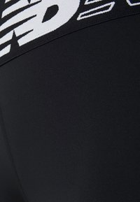 Czarne legginsy sportowe z teksturowanym pasem w kontrastującym białym logo. Gładki materiał o właściwościach elastycznych.