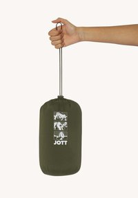 Olijfgroene trekkoord tas met een gladde textuur, voorzien van witte grafische ontwerpen en het woord "JOTT" aan de voorkant. Hand houdt de tas vast.