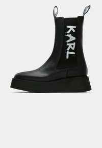 Bottines à plateforme noires en cuir avec des tirants et un panneau élastique latéral, arborant le texte blanc "KARL".