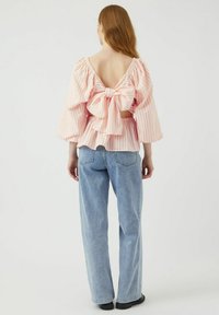 Blusa a righe rosa e bianca con scollatura a V profonda, maniche oversize e un grande fiocco in vita, abbinata a jeans azzurri chiari.