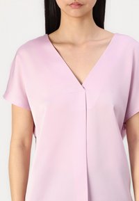 Blusa rosa chiaro con scollatura a V, maniche corte e silhouette rilassata. Realizzata in tessuto morbido con una leggera lucentezza.
