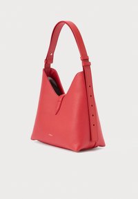 Czerwona skórzana torebka o uporządkowanym kształcie, z ostrymi górnymi krawędziami, regulowanym paskiem i subtelnym złotym logo u podstawy.