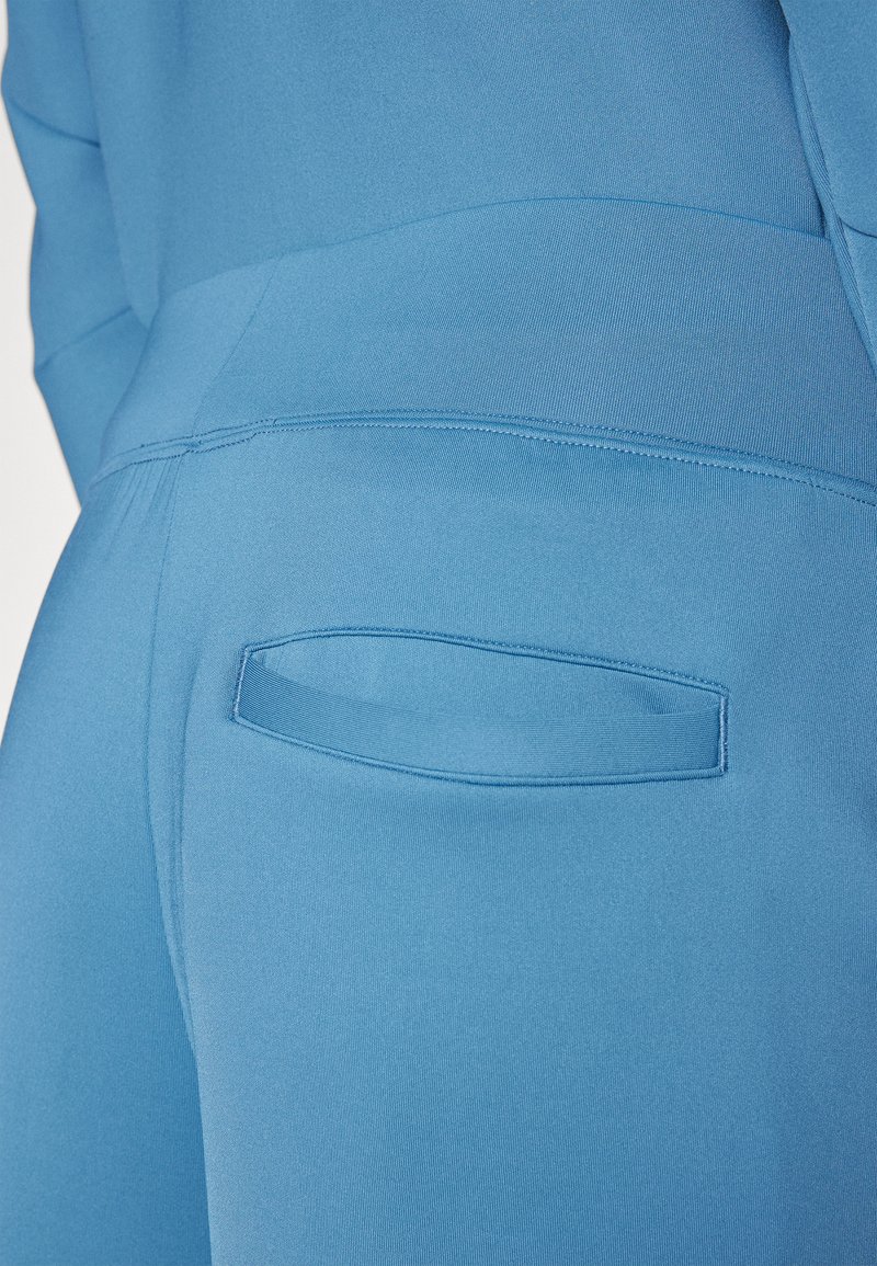 Primo piano di pantaloni di stoffa blu che mostrano una tasca posteriore con una fessura orizzontale e cuciture blu abbinate.