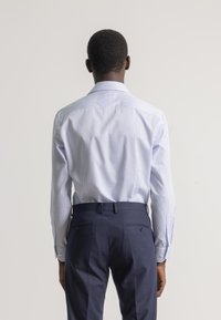 Camisa de vestir a rayas azul claro con mangas largas, cuello abotonado y pantalones náuticos en contraste con doble bolsillo trasero y botones.