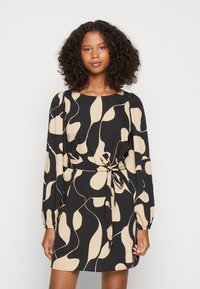 Vestido preto com um padrão abstrato bege, mangas longas, decote redondo e um detalhe na cintura amarrado. Tecido suave com um corte solto.